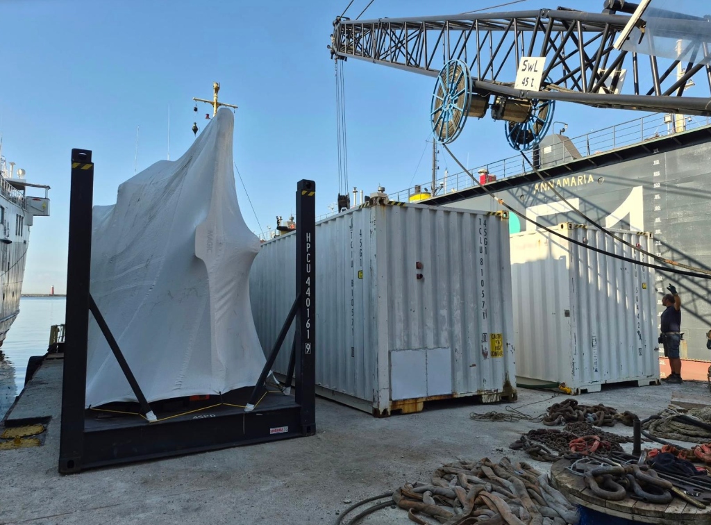 Shrink-wrapped yacht on flat rack container at port quay